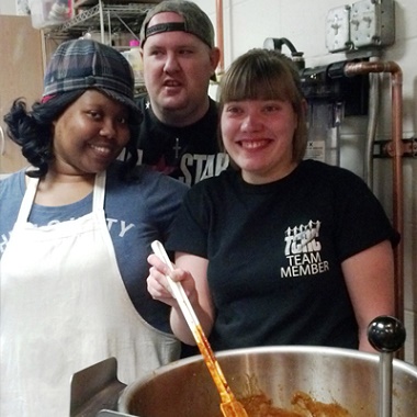 Three TCRC team members stand behind a big bowl of soup. 